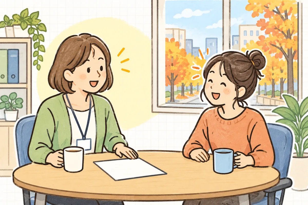 明るい事務所で、労務担当者と新しく社員になったデザイナーが、机をはさんで笑顔で話している場面